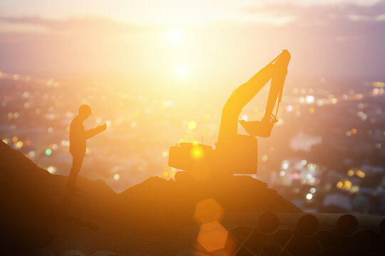 Silhouette excavator in construction site on sunset sky background and teams of business engineers looking for blueprints in construction sites, through blurry at sunset in industry success concept.