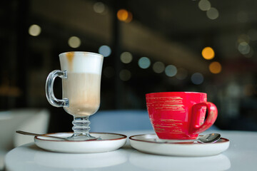 Fototapeta premium A cup of latte coffee and a cup of tea on a table in a coffee shop, the eternal dispute of tea or coffee.