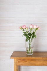 Vertical closeup of pink roses in glass vase on edge of oak table against wood panelled wall with copy space (selective focus)