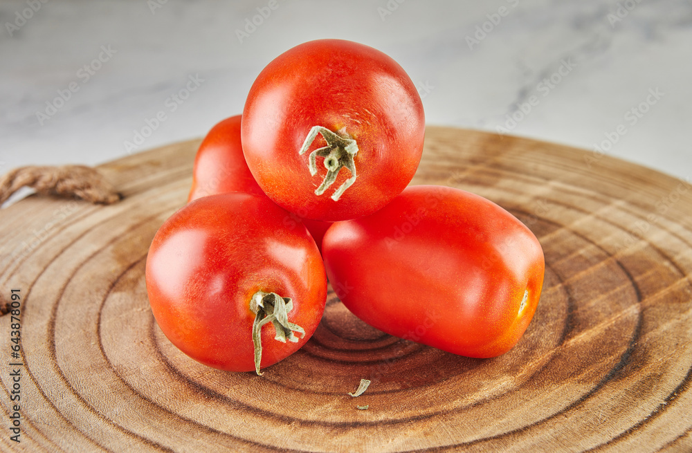 Poster Tomatoes plum stacked in hill on a wooden background on white marble