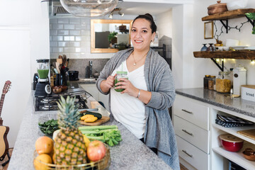 Young hispanic woman plus size drinking green juice in loft apartment kitchen in Mexico Latin America, mexican female at home