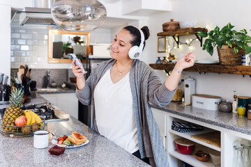 young latin woman plus size singing and dancing and using headphones in kitchen at home in Mexico...