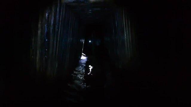 Digger person walking through dark tunnel adit, rain collector, sewer tunnel underground, illuminating light of lantern flashlight. Infrastructure of mine adit for underground river. Sewage collector