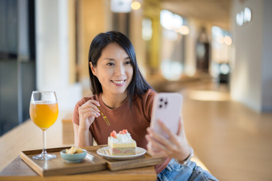 Woman take photo on cellphone with cake and drink in restaurant
