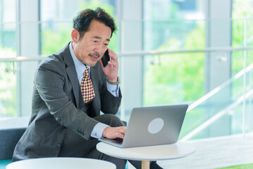 電話で話しながらパソコンを使うシニアビジネスマン