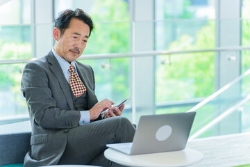 パソコンとスマートフォンを使いこなすシニアビジネスマン