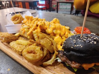 Wooden tray with different kinds of food placed with black burgers. Close-up view.
