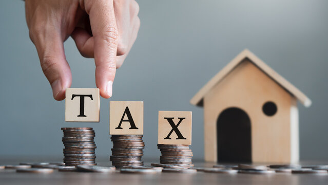 Property tax concept.Hand holding wooden block with TAX word on stack coin.Home background.Investment planning.business real estate.economy crisis.
