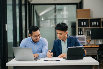 Two Asian businessman discuss investment project working and planning strategy with tablet laptop computer in modern office.
