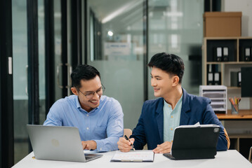 Two Asian businessman discuss investment project working and planning strategy with tablet laptop computer in modern office.