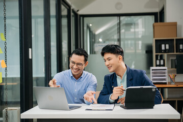 Two Asian businessman discuss investment project working and planning strategy with tablet laptop computer in modern office.