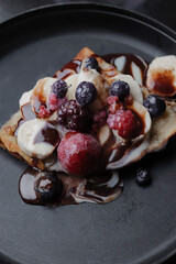 Vertical photo of sweet crepe, with chocolate and red berries, on a black plate.