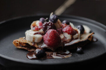 Close up of rich sweet rice flour crepe, with red berries, on a black plate