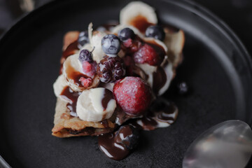 Sweet crepe, with red berries, on a black plate, homemade food for breakfast