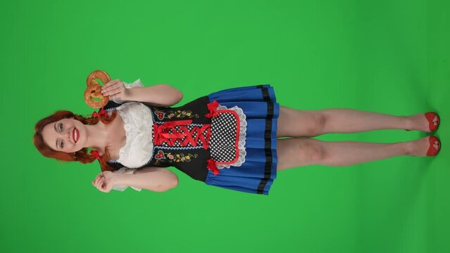 Full-size vertical green screen isolated chroma key video of a young German woman, waitress holding a pretzel, touching her cheeck and licking her lips.