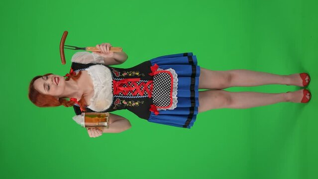 Full-size vertical green screen isolated chroma key video of a young German woman, waitress holding a wurst, sausage and a glass of beer. Wow and exitement.