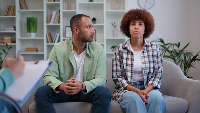 Unhappy married couple being on verge of family crisis visiting counselor to save relationships. Husband having word and blaming partner in problems when wife sitting still with angry face expression