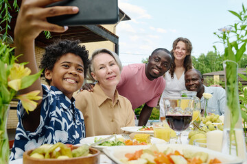 Happy large intercultural family looking at camera of smartphone held by cute smiling boy sitting in front of his parents and grandparents