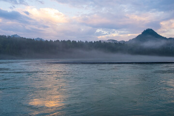 A wide, full-flowing mountain river with a fast current at dawn or sunset. Mountains and forest in the fog. A large turquoise-colored mountain river Katun in the Altai Mountains, Altai Republic.