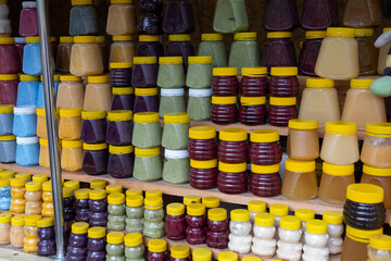 There are many jars of organic, natural honey on the counter for sale. Different honey, different colors in plastic cans are ready for sale at the honey fair. Nuts filled with honey. 