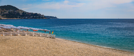 Fototapeta premium Pebble beach along Promenade des Anglais with beach umbrellas and chairs with the turquoise water of the Mediterranean Sea in Nice, Cote d'Azur France