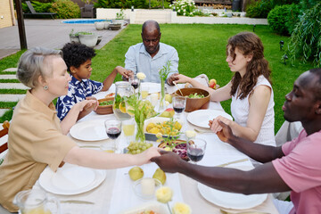 Large intercultural family of three generations holding by hands during pray while sitting by table served with homemade food and drinks