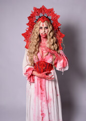 Close up portrait of  scary vampire zombie queen, wearing elegant halloween fantasy costume with crown and bloody red paint splatter. Isolated on studio background with gestural hands reaching out tow