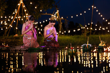 Two thai woman sitting wai on a raft by the river, Asian women in traditional Thai costumes bring krathongs to float on Loi Krathong Day, traditions and culture of Thailand,