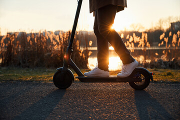 Man riding electric scooter in city park during autumn sunset
