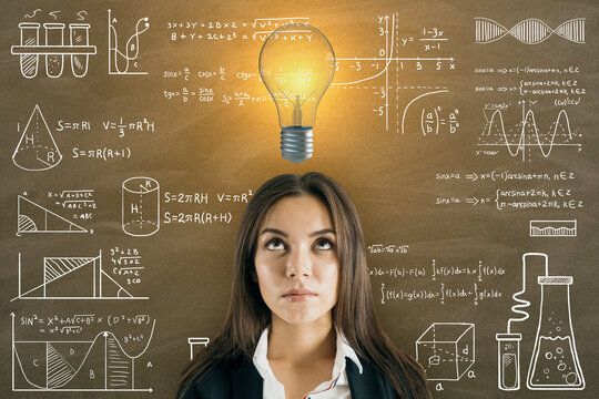 Portrait of attractive thoughtful young european businesswoman with glowing light bulb on chalkboard wall background with mathematical formulas. Science, idea and education background. - Powered by Adobe