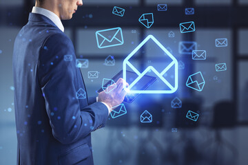 Businessman hands using tablet with glowing email letter icons on blurry office interior...