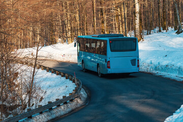 Tourist shuttle bus on the road through wooded landscape in winter