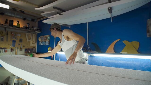 Male surfboard shaper making surfboard in his workshop. Hand shaping from blank.