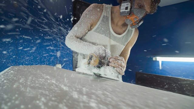 Male surfboard shaper making surfboard in his workshop. Hand shaping from blank.