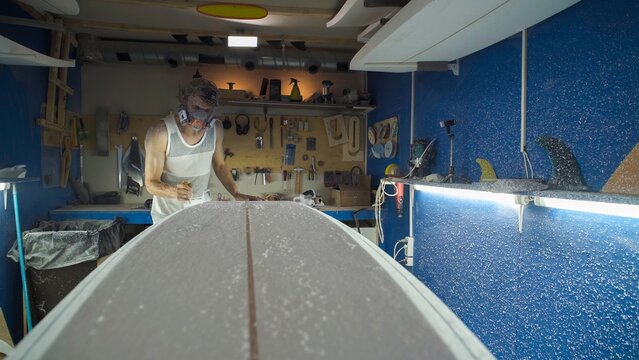 Male surfboard shaper making surfboard in his workshop. Hand shaping from blank.