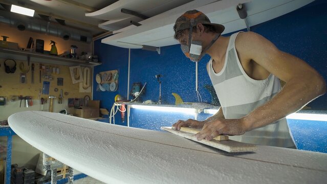 Male surfboard shaper making surfboard in his workshop. Hand shaping from blank.