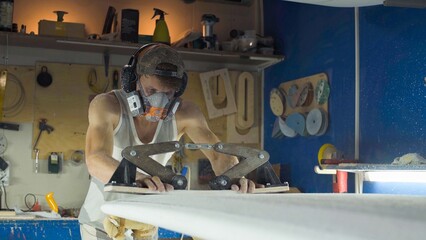 Male surfboard shaper making surfboard in his workshop. Hand shaping from blank.