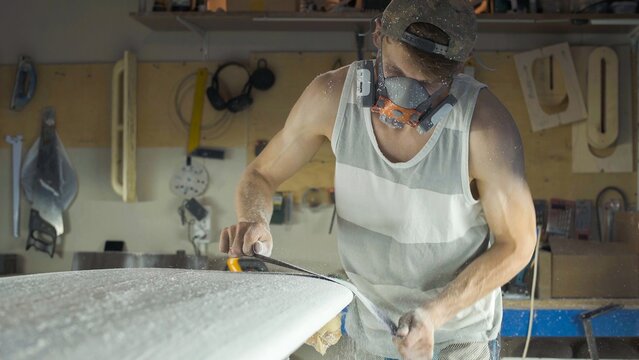 Male surfboard shaper making surfboard in his workshop. Hand shaping from blank.