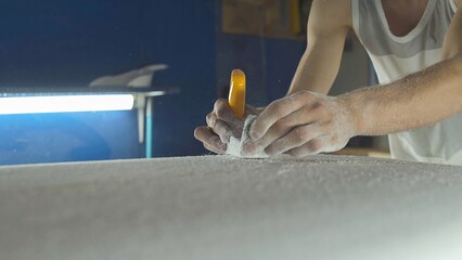Male surfboard shaper making surfboard in his workshop. Hand shaping from blank.