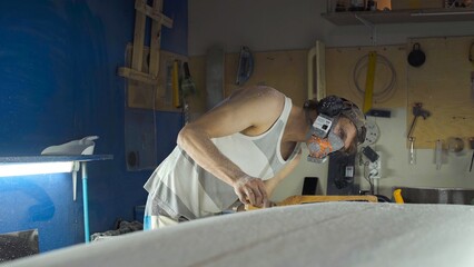 Male surfboard shaper making surfboard in his workshop. Hand shaping from blank.
