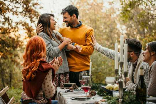 The joyous ambiance of a garden party, with a couple proposal with a diverse group of people relishing a shared meal amidst nature's beauty. - Powered by Adobe