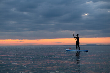 SUP. Stand up shovel. Adventurous girl on the paddle board rows during a bright and vibrant sunset.Silhouette of woman paddleboarding at sunset. Canakkale, Türkiye.