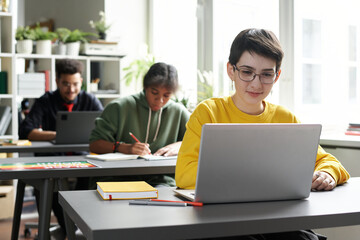Student sitting at desk and using laptop in her study during lesson in class