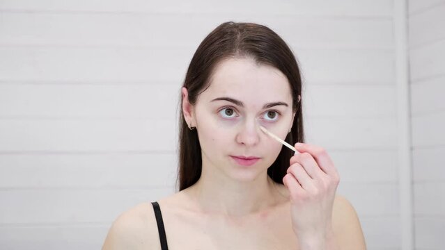 Woman does natural makeup applying concealer on flawless fresh skin. Girl looking at mirror. Put corrector under eye area. Beauty face, skincare. Copy space, advertising. Morning visage preparation.