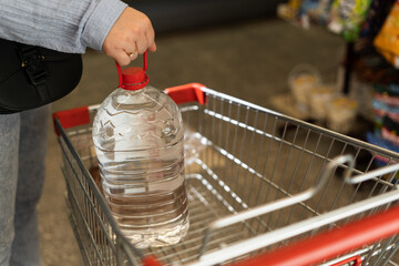 Woman buy big plastic bottle of drinking water in store and putting it in shopping cart