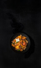 Fusilli pasta with mushrooms, asparagus and cherry tomatoes on a modern design plate with dark background