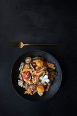 Fusilli pasta with mushrooms, asparagus and cherry tomatoes on a modern design plate with dark background