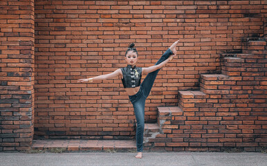 Fototapeta na wymiar Ballet dancer woman on brick wall background. Ballerina girl. Young athletic girl dancing leaping in the air. Concept of art, sport, sportive life.Jump Twine. Doing sport outside