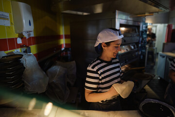 Fototapeta premium Young Woman Working Pizza Dough at Pizzeria