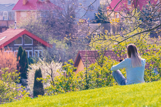 The girl sits on a hill on a green spring lawn and enjoys the spring.